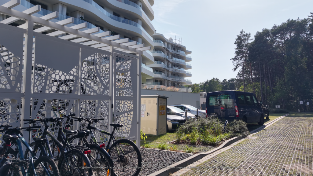 droga z ekokraty przy budynku apartamentowym z rowerownią i zaparkowanymi samochodami