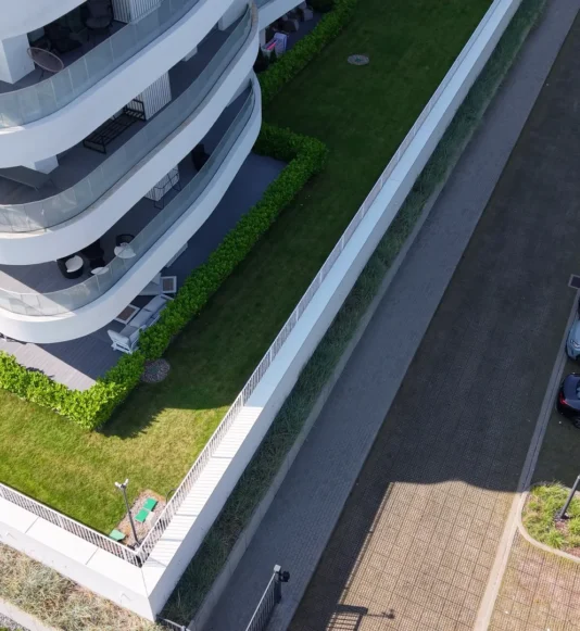 Widok z drona na nowoczesny budynek mieszkalny z zielonym pasem trawy i parkingiem z nawierzchnią ażurową