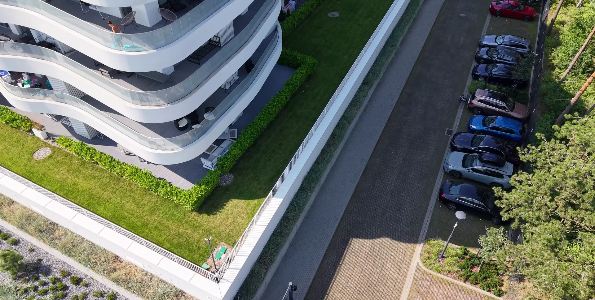Widok z drona na nowoczesny budynek mieszkalny z zielonym pasem trawy i parkingiem z nawierzchnią ażurową